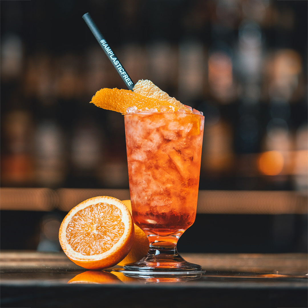 #IAMPLASTICFREE Trinkhalm in Absinthe-Glas mit orangem Cocktail, crushed Ice und Orangenzeste, dabei eine halbierte Orange