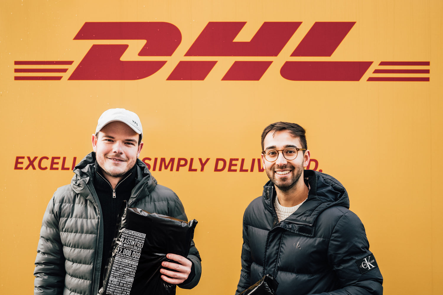 #IAMPLASTICFREE Gründer Daniel Knoeppel (links) und Kevin Mata (rechts) vor DHL Auto mit Versandtasche in der Hand