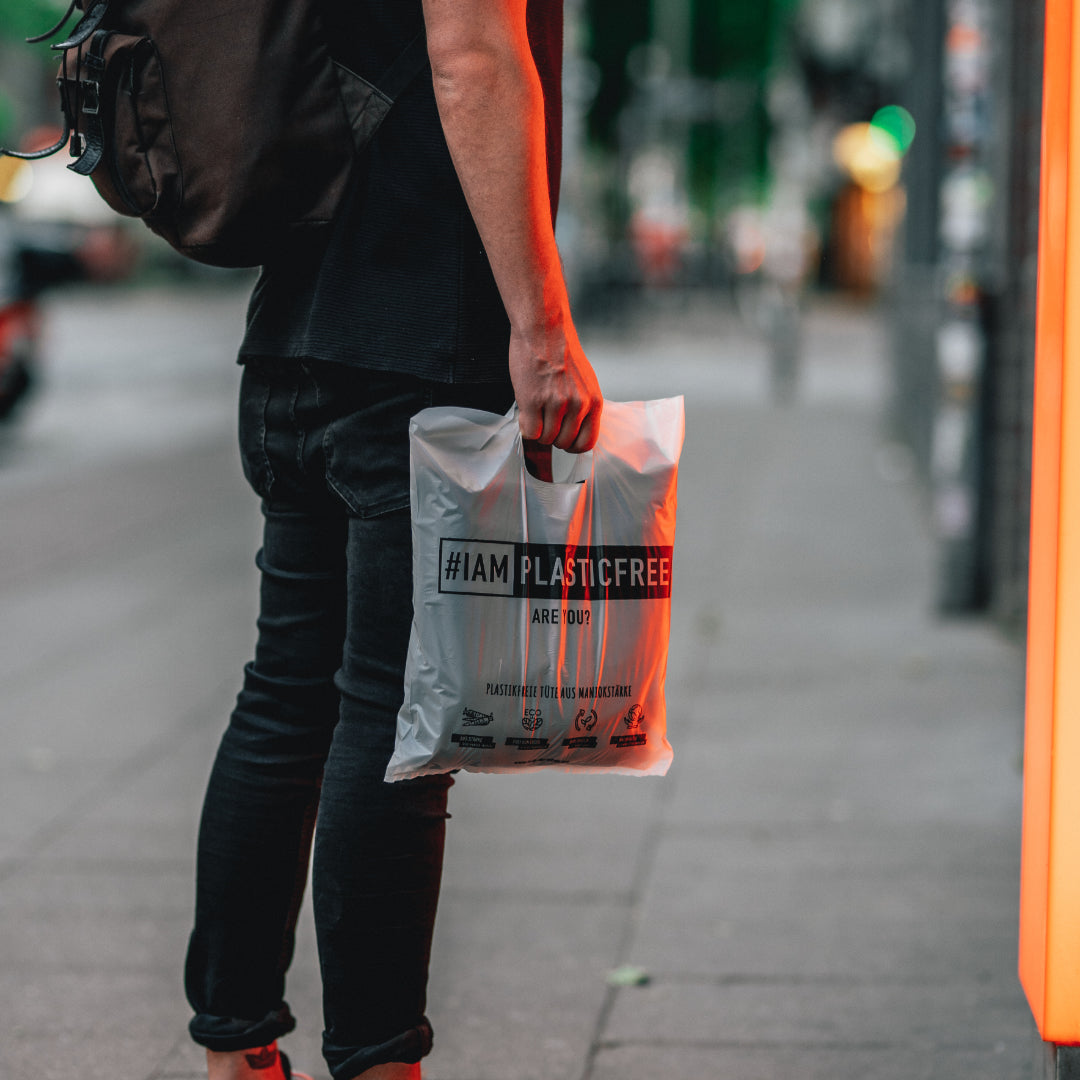 #IAMPLASTICFREE Shopping Bag Einkaufstüte von Person gehalten, neben Schaufenster mit orangem Licht