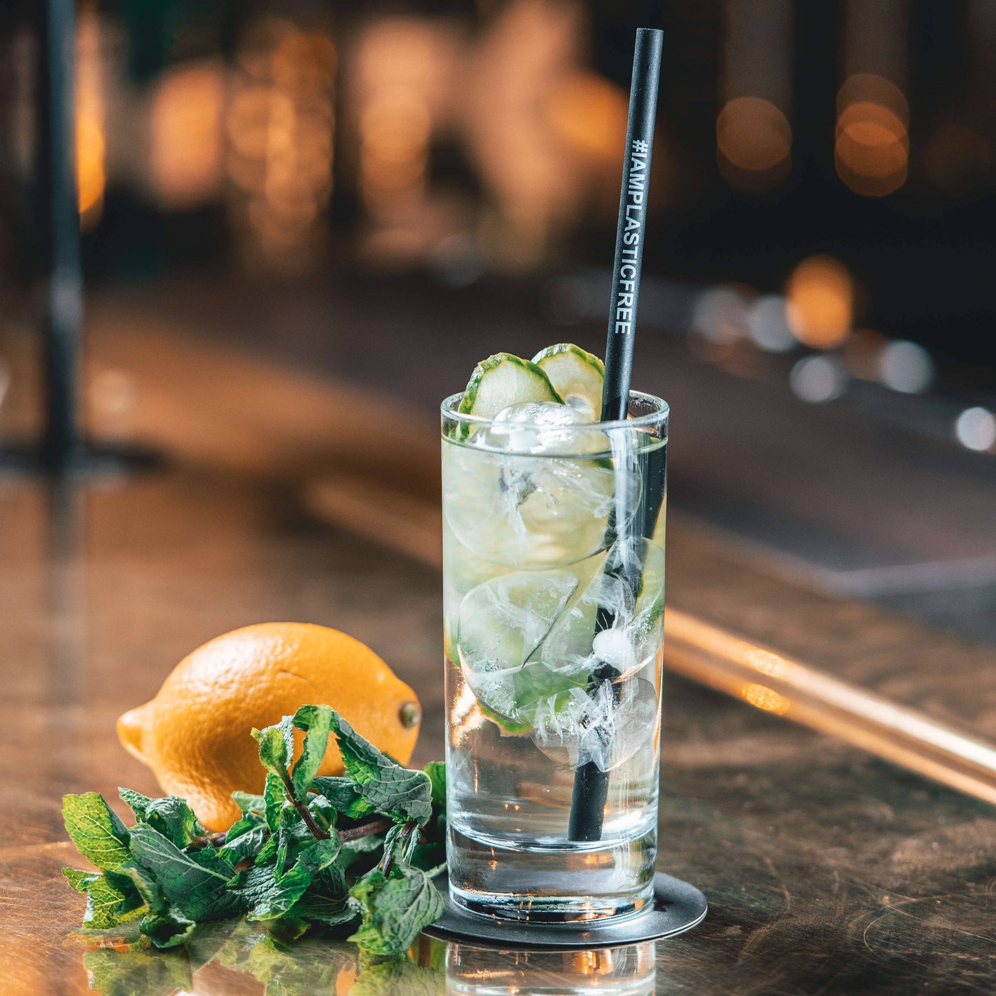 #IAMPLASTICFREE Trinkhalm 2.0 in Highball Glas mit klarem Cocktail, Eis und Gurkenscheiben, dazu Orange und Minzzweig